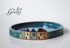 a small blue plate with houses painted on it's sides and the words art gretta above it