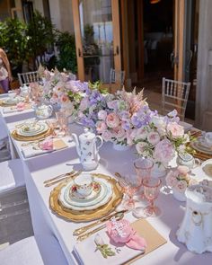 the table is set with pink and white flowers in vases, china dishes, and plates