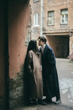 a man and woman standing next to each other near a brick wall in an alleyway