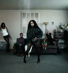 a group of people in a living room with one woman dancing and the other standing