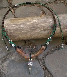 a necklace with a long horn and beads is on the ground next to a piece of wood