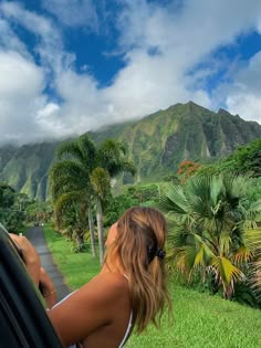 a woman looking out the window of a car on a tropical road with palm trees and mountains in the background