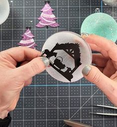 two hands are holding a christmas ornament in front of some crafting supplies