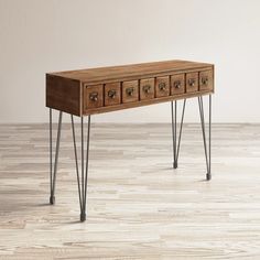 a wooden table with four drawers and hairpinks on the legs, against a white wall