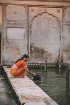 a woman in an orange shirt is sitting on the edge of a dock and holding a bucket