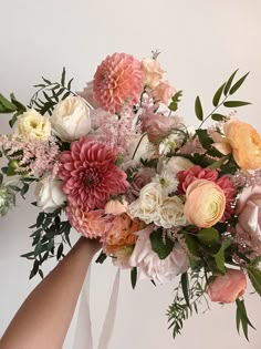 a bouquet of flowers being held by someone's hand in front of a white wall