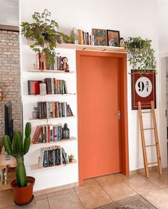 an orange door in a white room with bookshelves and plants on the shelves