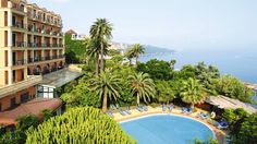 an outdoor swimming pool surrounded by trees next to a building with balconies and palm trees