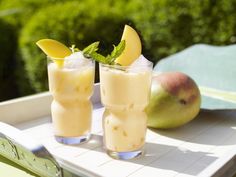 two glasses filled with drinks sitting on top of a white tray next to some fruit