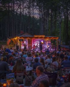 a large group of people sitting in front of a tent at night with lights on