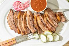 a white plate topped with meat and veggies next to a bowl of sauce