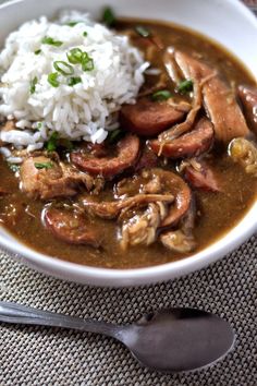 a white bowl filled with meat and rice on top of a table next to a spoon