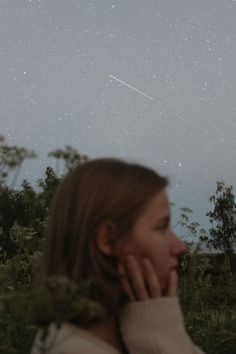 a woman is looking up at the stars in the sky above her head while she holds her hand to her face