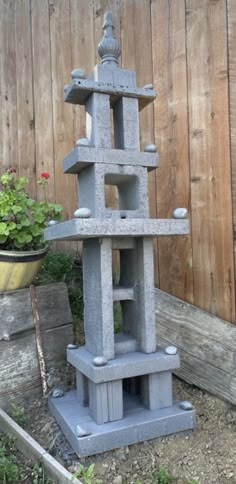 a cement sculpture sitting in the middle of a garden next to a wooden fence and potted planter