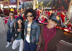 some kids are standing in front of a roller coaster at an amusement park and posing for the camera