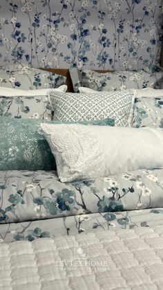 a bed with blue and white flowers on the comforter, pillows and pillow cases