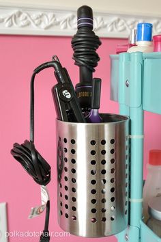 a hair dryer and other items in a metal container on a shelf next to a pink wall