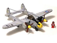 a lego airplane with a man standing next to it on a white surface in front of the plane