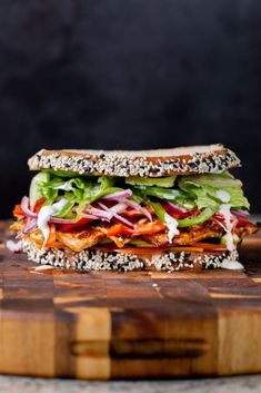 a sandwich with lettuce, tomato, and other toppings on a cutting board