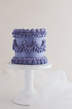 a three tiered cake with purple icing on a white pedestal, sitting on a table