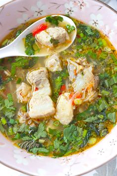 a bowl of soup with meat and greens on the side, next to a spoon