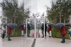 several people with umbrellas standing in front of a glass enclosure on the side of a road