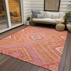 an orange and pink rug sitting on top of a wooden floor next to a white couch