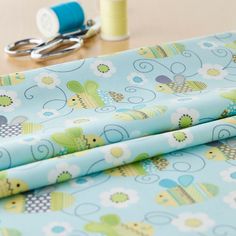 scissors and thread are sitting on a table next to a blue background with green, yellow, and white flowers