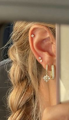 a woman wearing gold ear cuffs and piercings in her hair is looking at the mirror