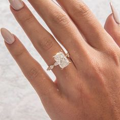 a woman's hand with an engagement ring on it and her nails in the foreground