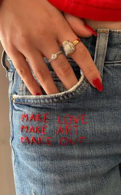 a woman's hand with red nail polish holding onto her jeans that says make love make art make out