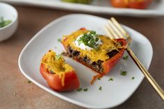 two stuffed peppers on a white plate with a fork next to it and another dish in the background