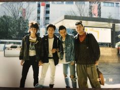 three young men standing next to each other in front of a building with tall buildings