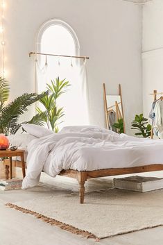 a bedroom with white linens and plants in the corner