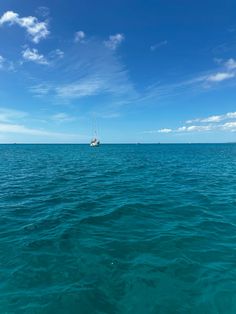 a sailboat floating in the ocean under a blue sky with wispy clouds