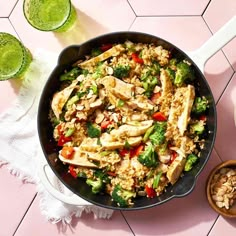 a skillet filled with chicken and vegetables on top of a pink tile countertop