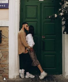 a man and woman kissing in front of a green door