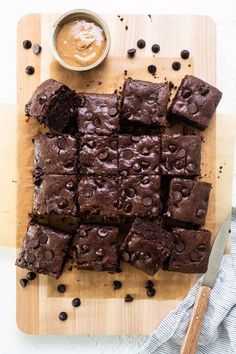 chocolate brownies cut into squares on a cutting board with a bowl of peanut butter