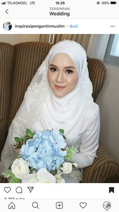 a woman in a white hijab holding a bouquet of blue and white flowers