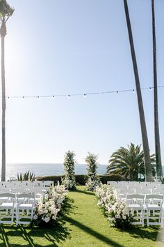 an outdoor ceremony set up with white chairs and flowers on the lawn next to the ocean