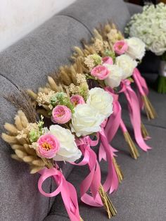 three bouquets of flowers are sitting on a gray couch with pink ribbons around them