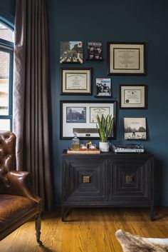 a living room with blue walls and pictures on the wall above an old leather chair