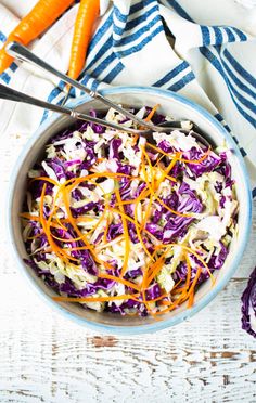 a bowl filled with coleslaw and carrots on top of a white table