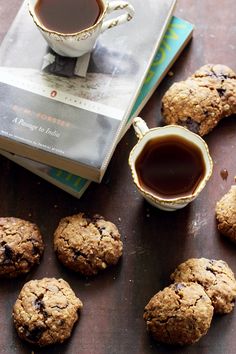 chocolate chip cookies next to a cup of tea and a book on a wooden table