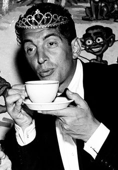 a black and white photo of a man wearing a tiara drinking from a cup