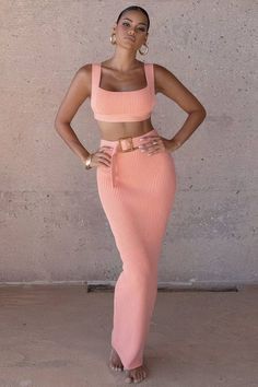 a woman standing in front of a wall with her hands on her hips and wearing a pink crop top