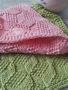 two knitted blankets sitting next to each other on top of a wooden table with an egg in the background