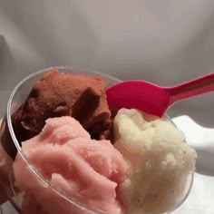 three scoops of ice cream in a plastic cup with a spoon on top and two different flavors