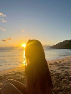 a woman sitting on top of a sandy beach next to the ocean at sun set