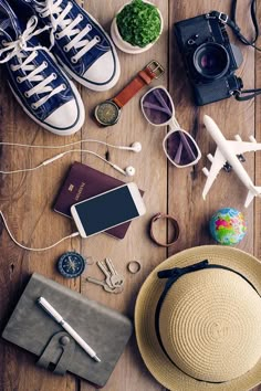 an assortment of personal items laid out on a wooden table with sunglasses, camera, passport, cell phone and other accessories